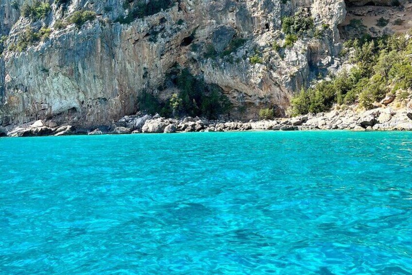 Clear turquoise water, rocky cliffs, and sparse vegetation. 3