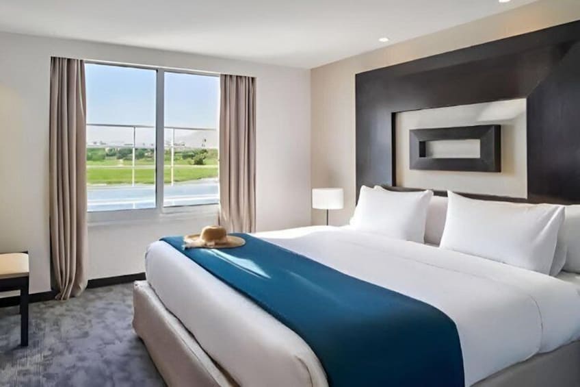 A hotel room with a large bed, a view of a green landscape through the window, and a modern wall design. 2