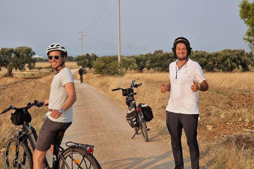 Deux personnes sur une route de campagne, à vélo, entourées d’herbe sèche et d’arbres. 1