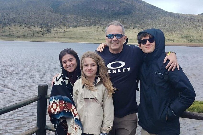 Un grupo de personas de pie junto a un lago con un paisaje montañoso al fondo. 1