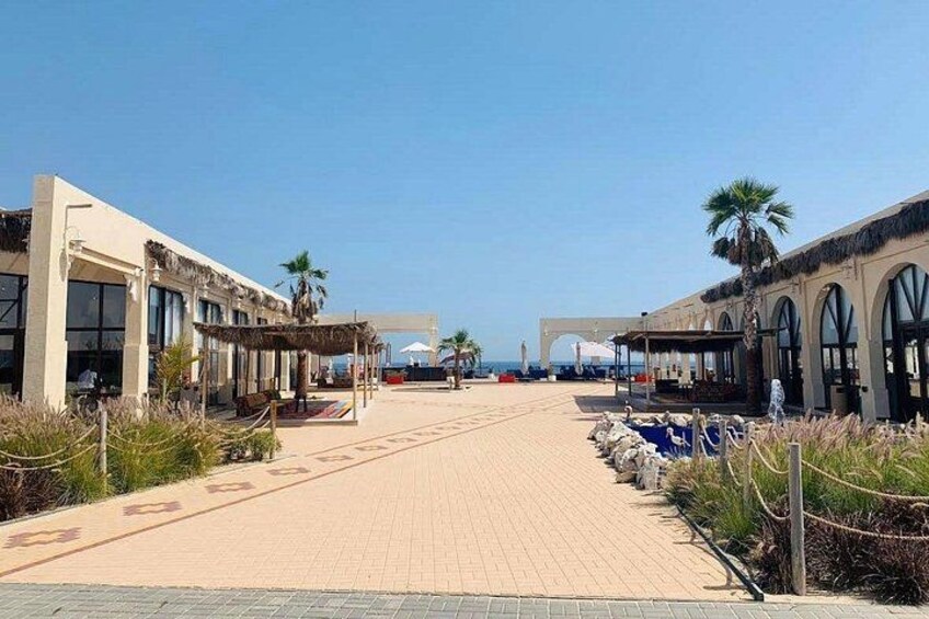 A paved walkway with buildings on either side, palm trees, and a clear sky. 3