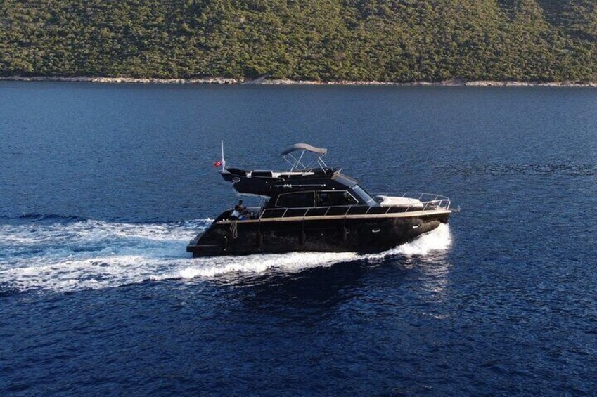 Un velero negro con una bandera en la proa, navegando sobre el agua con una costa arbolada al fondo. 1