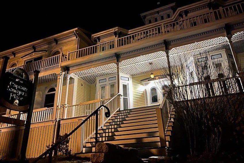 A historic building with a porch, stairs, and a sign. 2