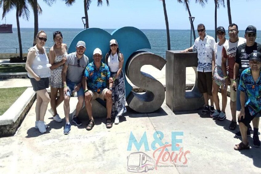 Een groep mensen poseert voor een groot blauw beeld met de letters 'M&F' en 'Tours'. 4