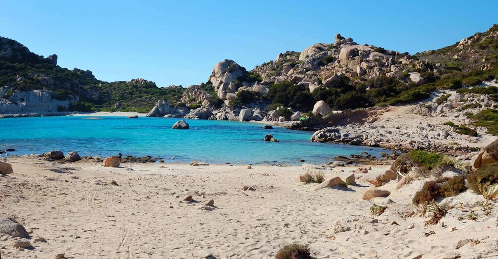 A beach with clear turquoise water, rocky outcrops, and sparse vegetation. 4