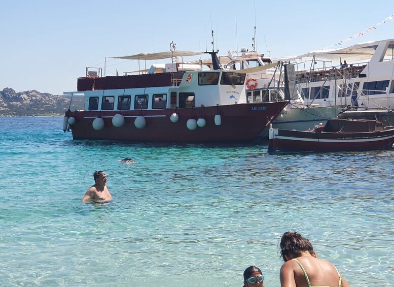 A clear blue sea with people swimming and a large boat docked. 2