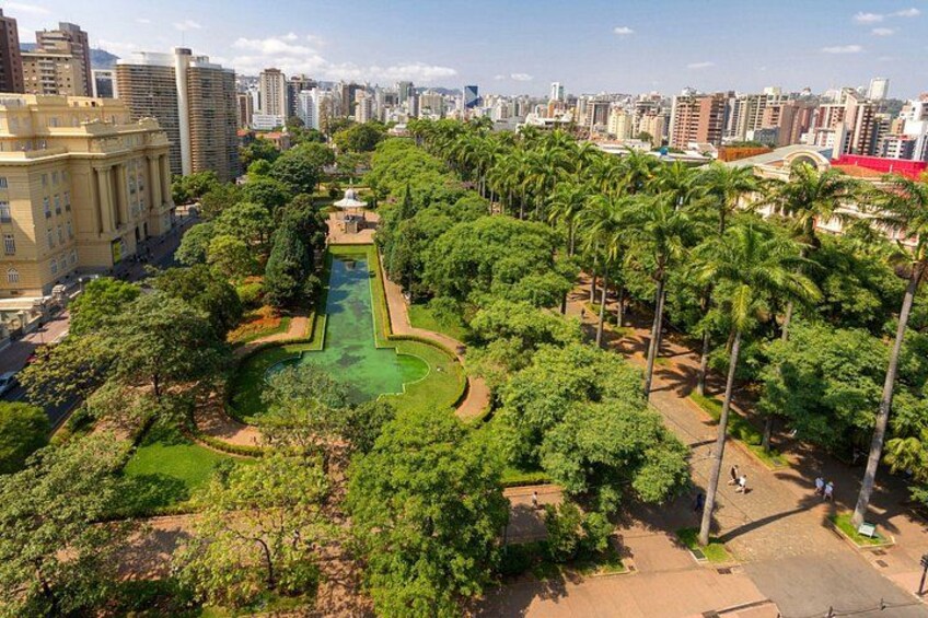 A park with a central pond, surrounded by trees and pathways, with buildings in the background. 3