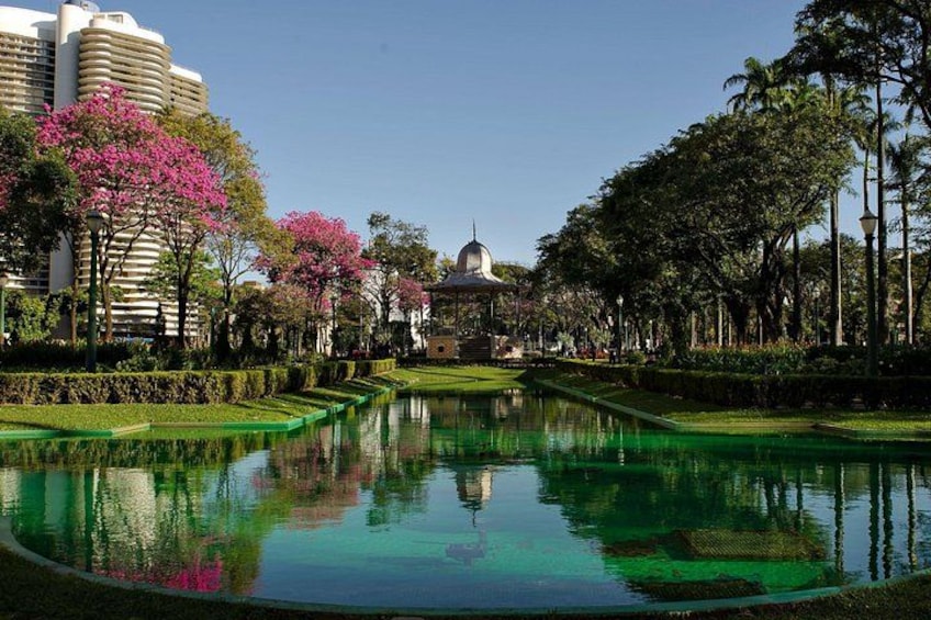 A tranquil garden with a reflective pond, lush greenery, and a prominent building with a dome in the background. 1