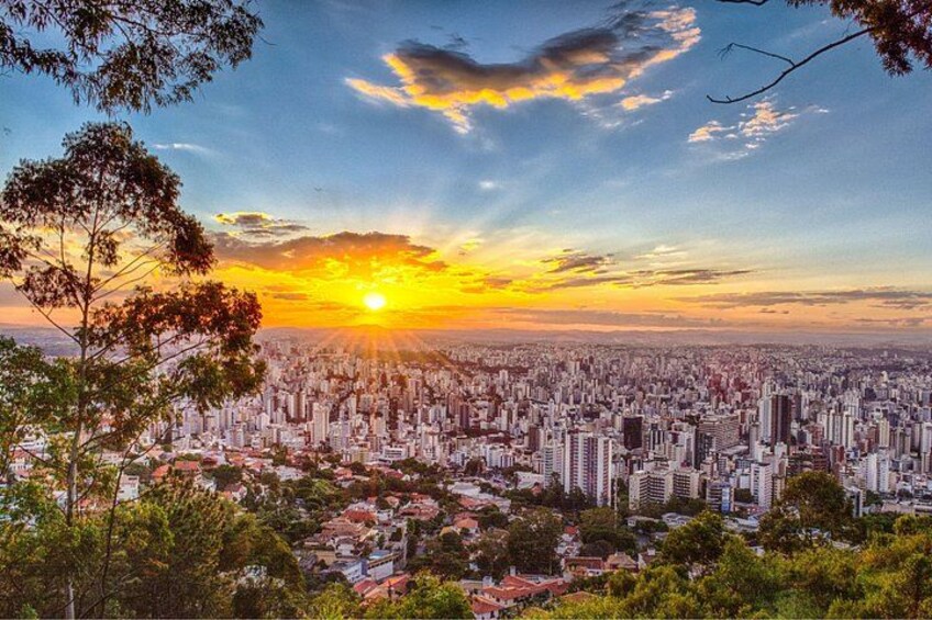 A cityscape at sunset with a dense urban area, a prominent sun, and a tree in the foreground. 2
