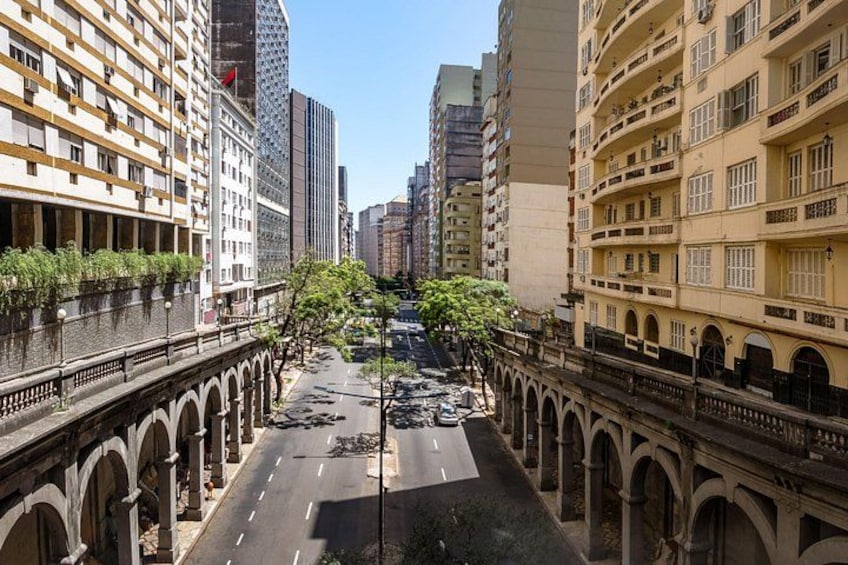 A city street lined with multi-story buildings, a bridge, and a clear sky. 4