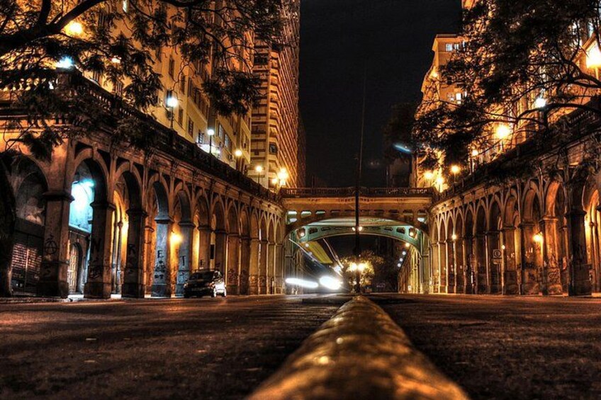 A nighttime cityscape with illuminated buildings, a bridge, and a road leading into the distance. 3
