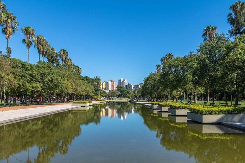 A calm lake with a reflection, surrounded by trees and a park with benches. 1