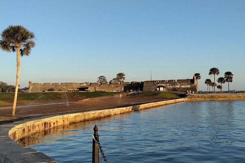 A coastal fortification with a palm tree, calm water, and clear skies. 1