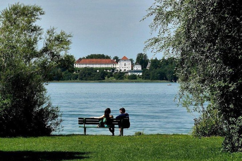A lake with a bench, two people sitting, and a large building in the background. 4