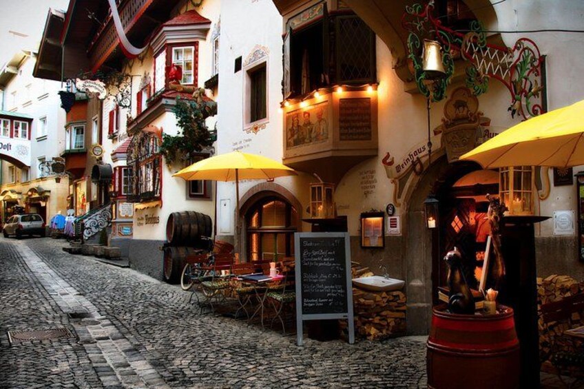A cobblestone street with a restaurant, outdoor seating, and a beer tap. 2