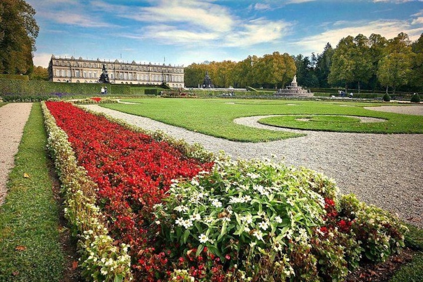 A formal garden with manicured lawns, flower beds, and a large building in the background. 1