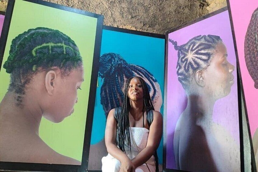 A person seated with framed portraits of individuals with braided hairstyles. 4