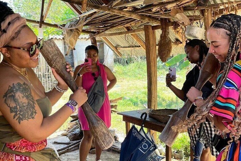 A group of people in a rustic outdoor setting, possibly a market or gathering, with wooden structures and natural surroundings. 3