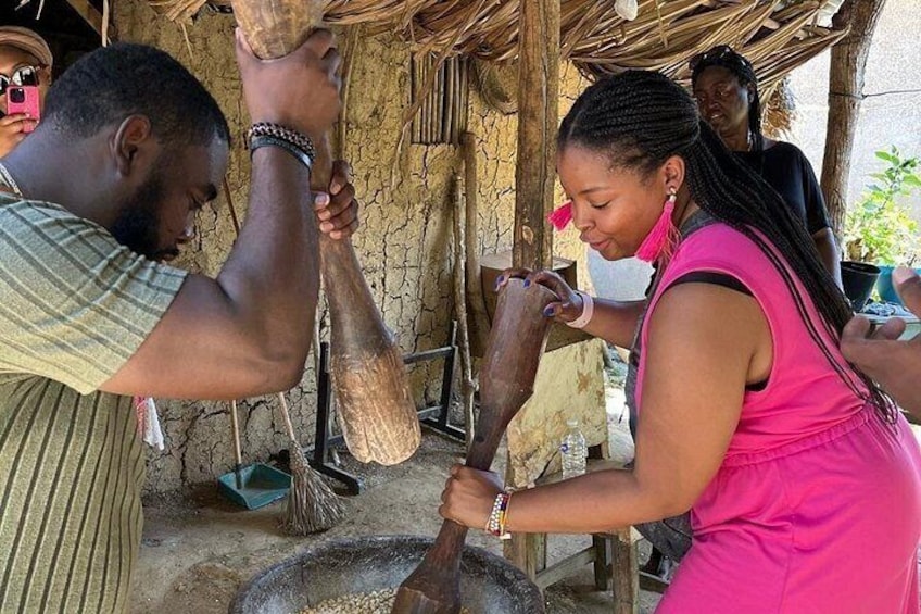 A person pounding grain with a wooden pestle in a rustic setting. 1