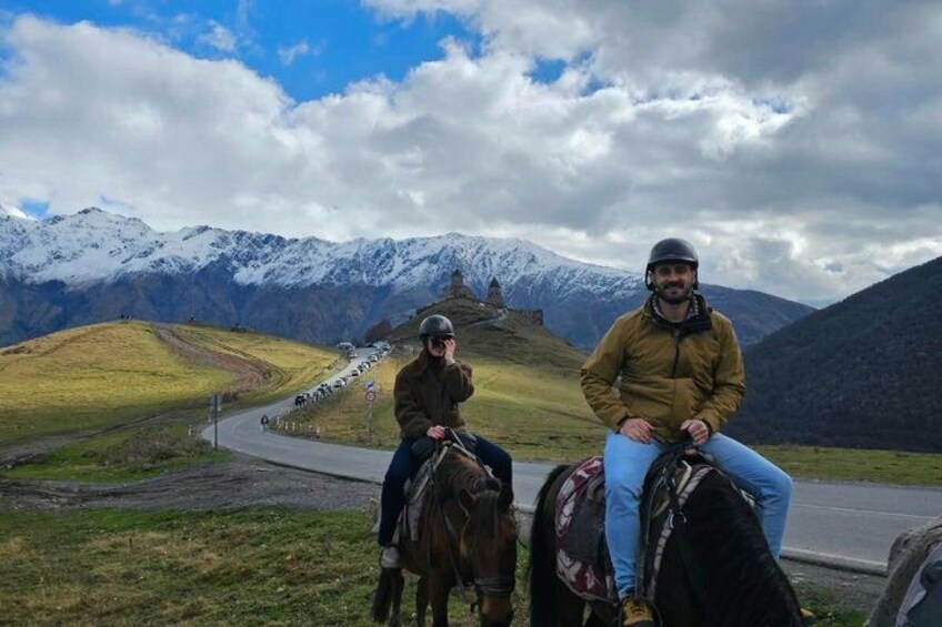 Two people on horseback on a road with mountains in the background. 5