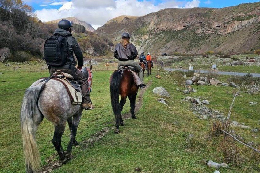 A group of people on horseback in a grassy area with a river and mountains in the background. 2