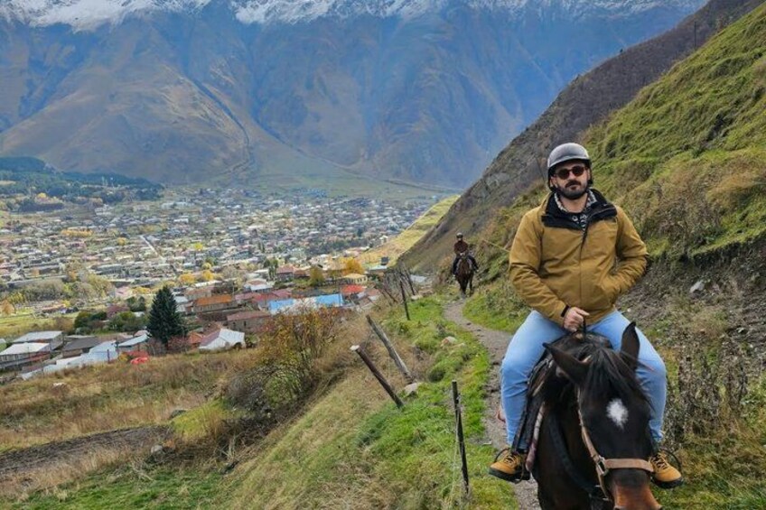 A person riding a horse on a mountain path with a village in the valley below. 3