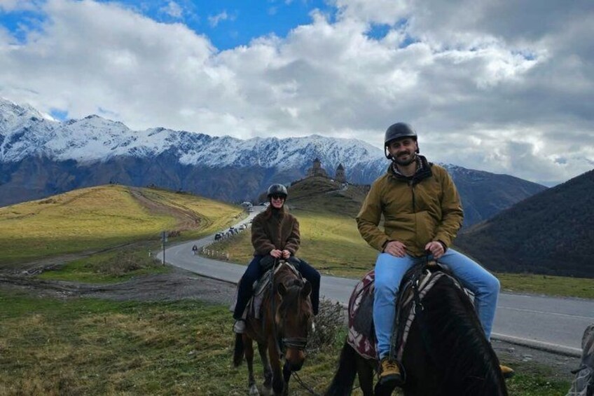 Two people on horseback on a road with mountains in the background. 4