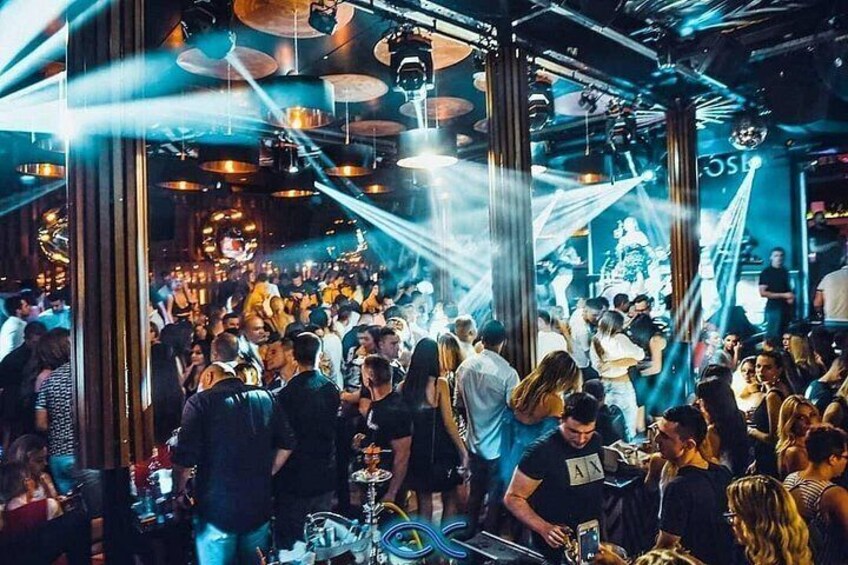 Un espace intérieur bondé, rempli de monde, avec des tables et une cabine de DJ. 3