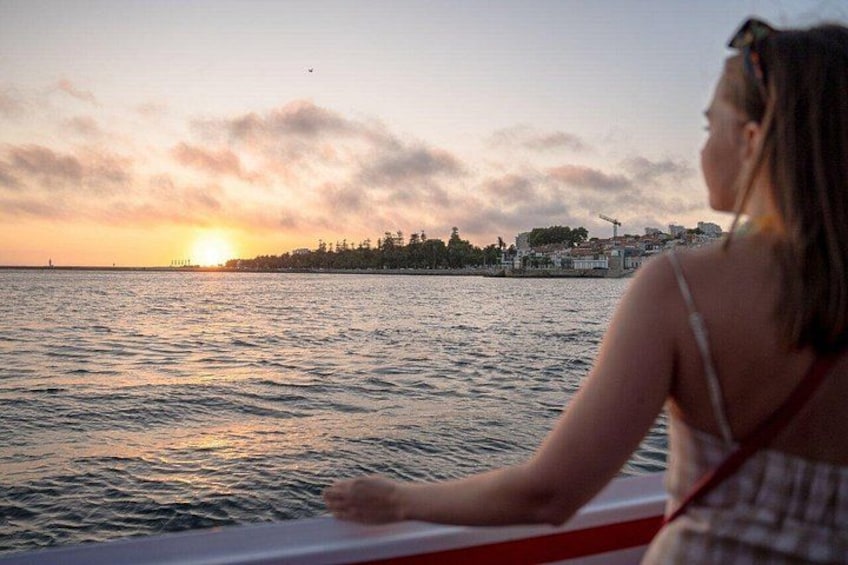 Eine Person in einem Boot bei Sonnenuntergang, im Hintergrund eine Stadtansicht und Wasser. 4