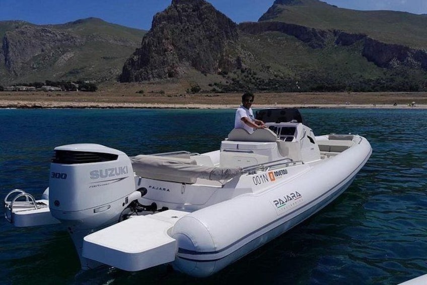 A white motorboat with a Suzuki 300 engine on calm water, a person on board, and a mountainous landscape in the background. 3