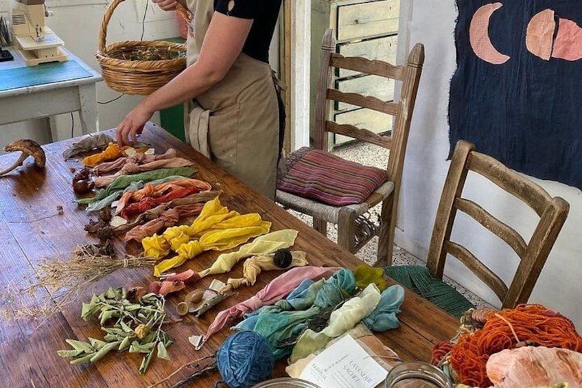 Een persoon die kleurrijke stoffen op een tafel rangschikt, met een mand en een stoel op de achtergrond. 3