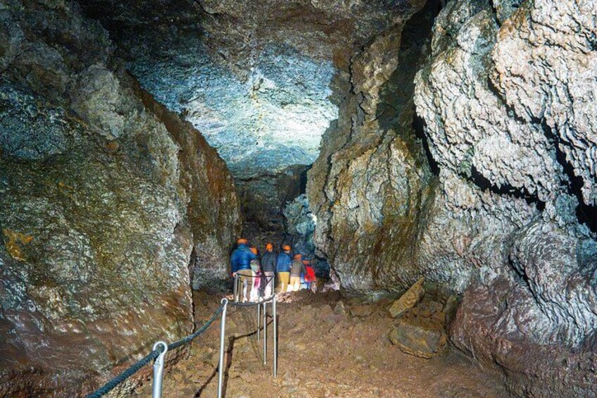A cave with stalactites, a rope ladder, and people exploring. 5