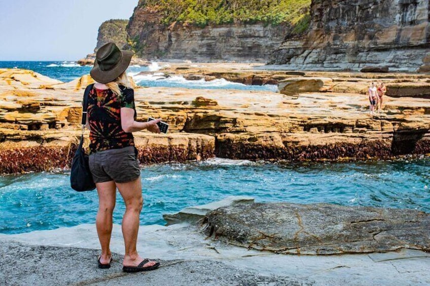 A person standing on rocky terrain near a body of water, with cliffs in the background. 4