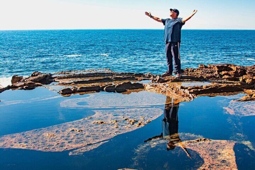A person standing on a rocky outcrop with arms outstretched, overlooking a body of water. 5