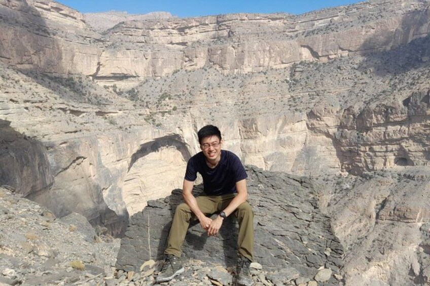 A person sitting on a rocky outcrop in a canyon with layered rock formations. 4