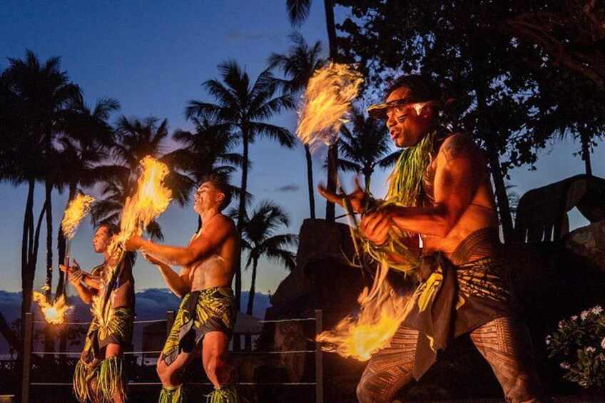 A person performing fire dancing with flaming poi in a tropical setting with palm trees. 1