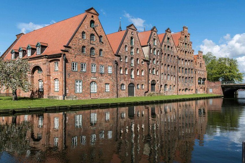 A large brick building with a red roof, a reflection in the water, and a bridge in the background. 3