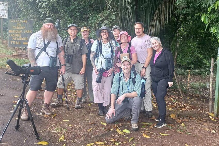 A group of people in outdoor gear posing in a natural setting with a camera on a tripod. 2