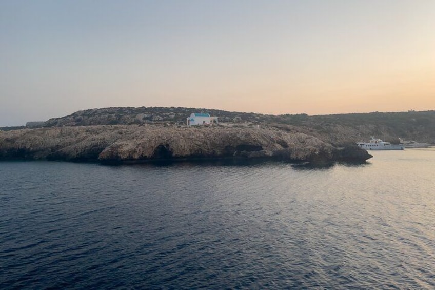 Un paysage côtier avec une île rocheuse, un bâtiment blanc et un bateau sur l’eau. 3