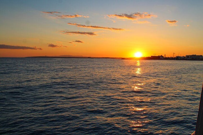 Un coucher de soleil sur une mer calme, avec la silhouette d’une ville à l’horizon. 2