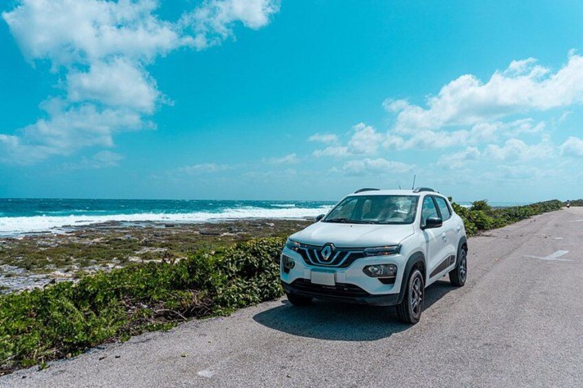 A white SUV parked on a coastal road with ocean and greenery in the background. 2