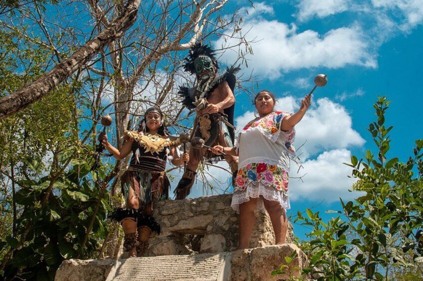 A group of people in traditional attire on a stone platform with trees and a clear sky in the background. 4