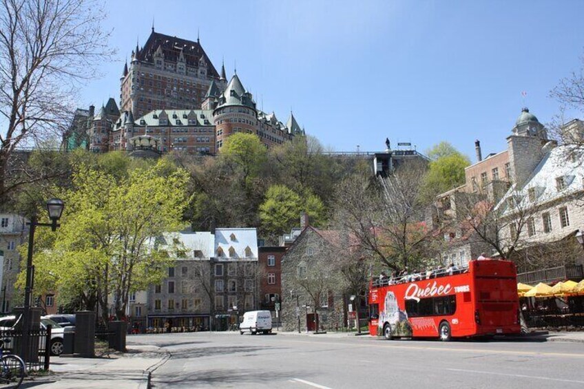 A red double-decker bus with 'Quebec' written on it, a historic building in the background, and a clear blue sky. 5