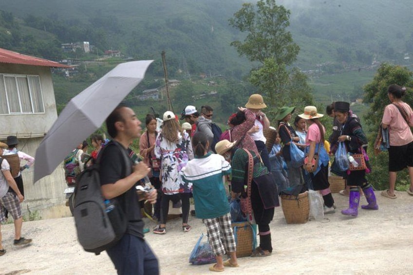A group of people standing on a hillside, some holding umbrellas, with a mountainous landscape in the background. 3