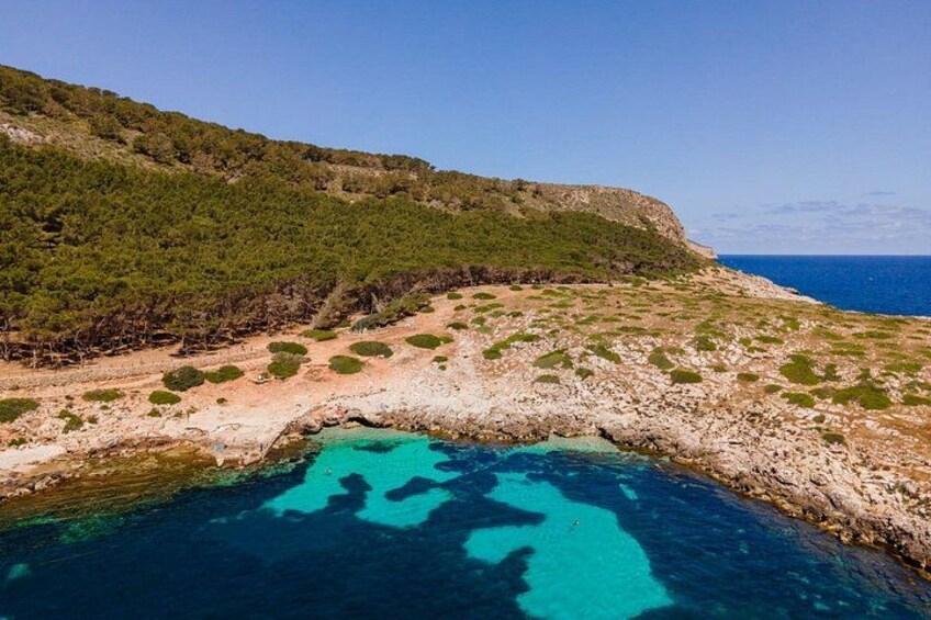 A coastal landscape with a rocky shoreline, a turquoise sea, and a green hill with sparse vegetation. 5