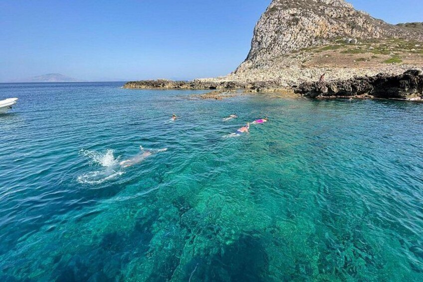 Clear blue sea, swimmers, and rocky coastline. 2