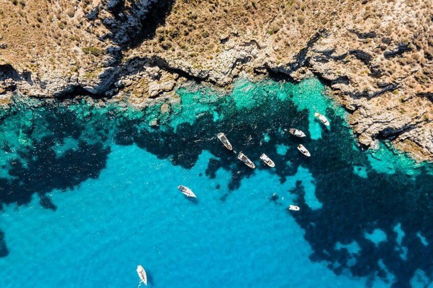 A coastal area with clear turquoise waters, rocky terrain, and several small boats anchored near the shore. 4