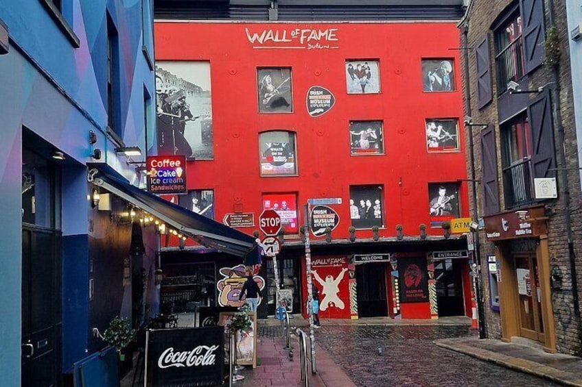 A street with a red building labeled 'Wall of Fame,' a Coca-Cola sign, and a stop sign. 4