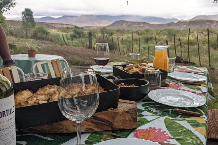 Una mesa al aire libre con comida, copas de vino y una botella. 1