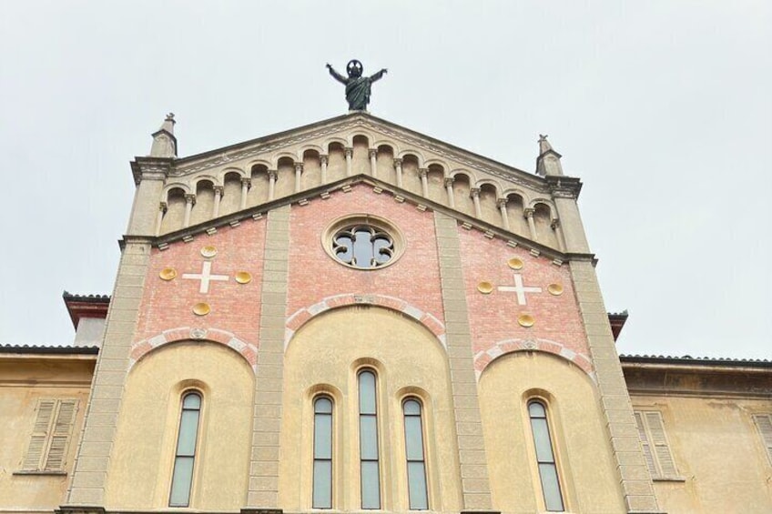 Una iglesia con una estatua en la parte superior, ventanas en arco y cruces en la fachada. 3